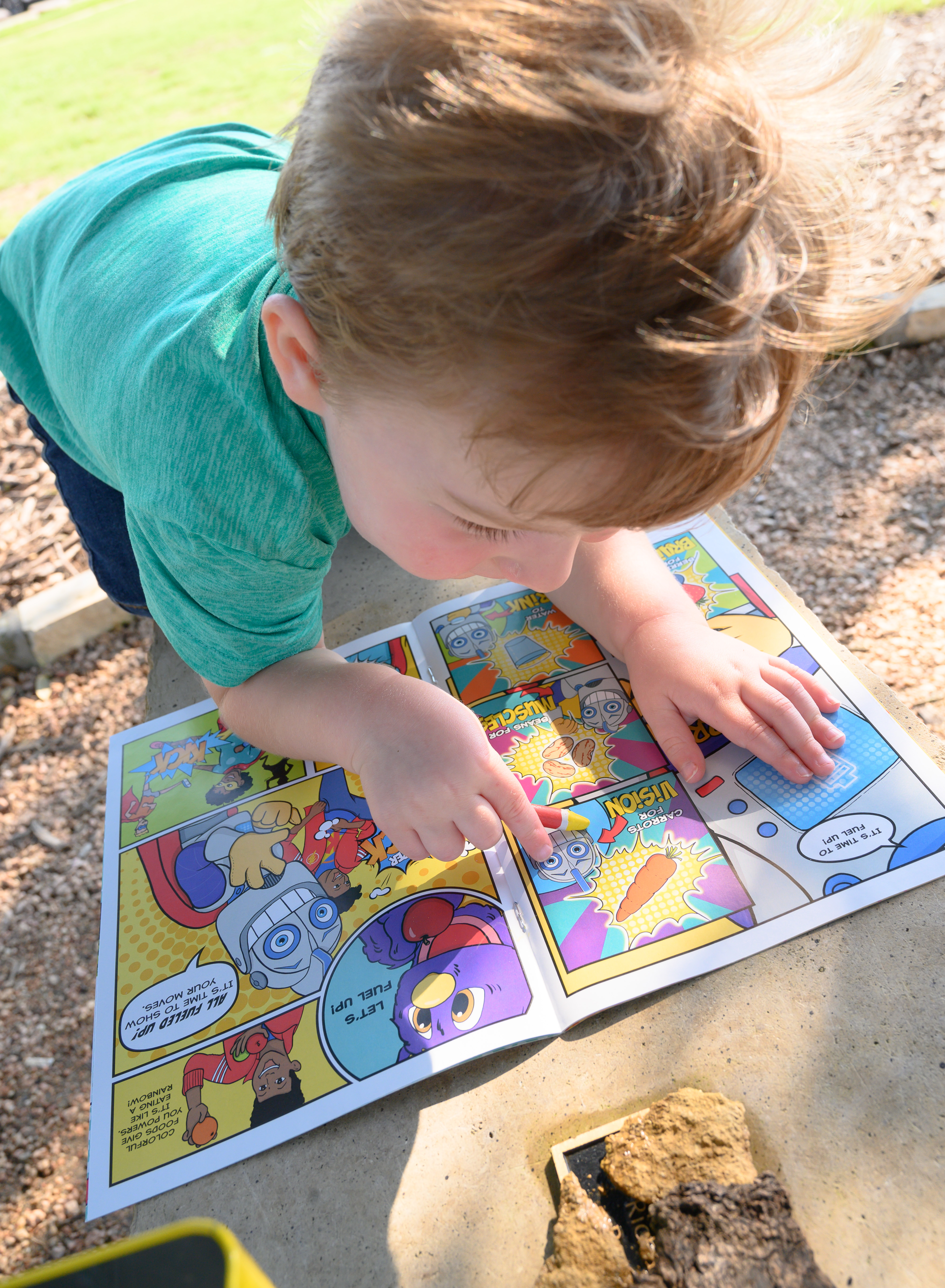 Un niñito afuera señalando una imagen en el libro de historietas, Campamento para Entrenar Superhéroes 
