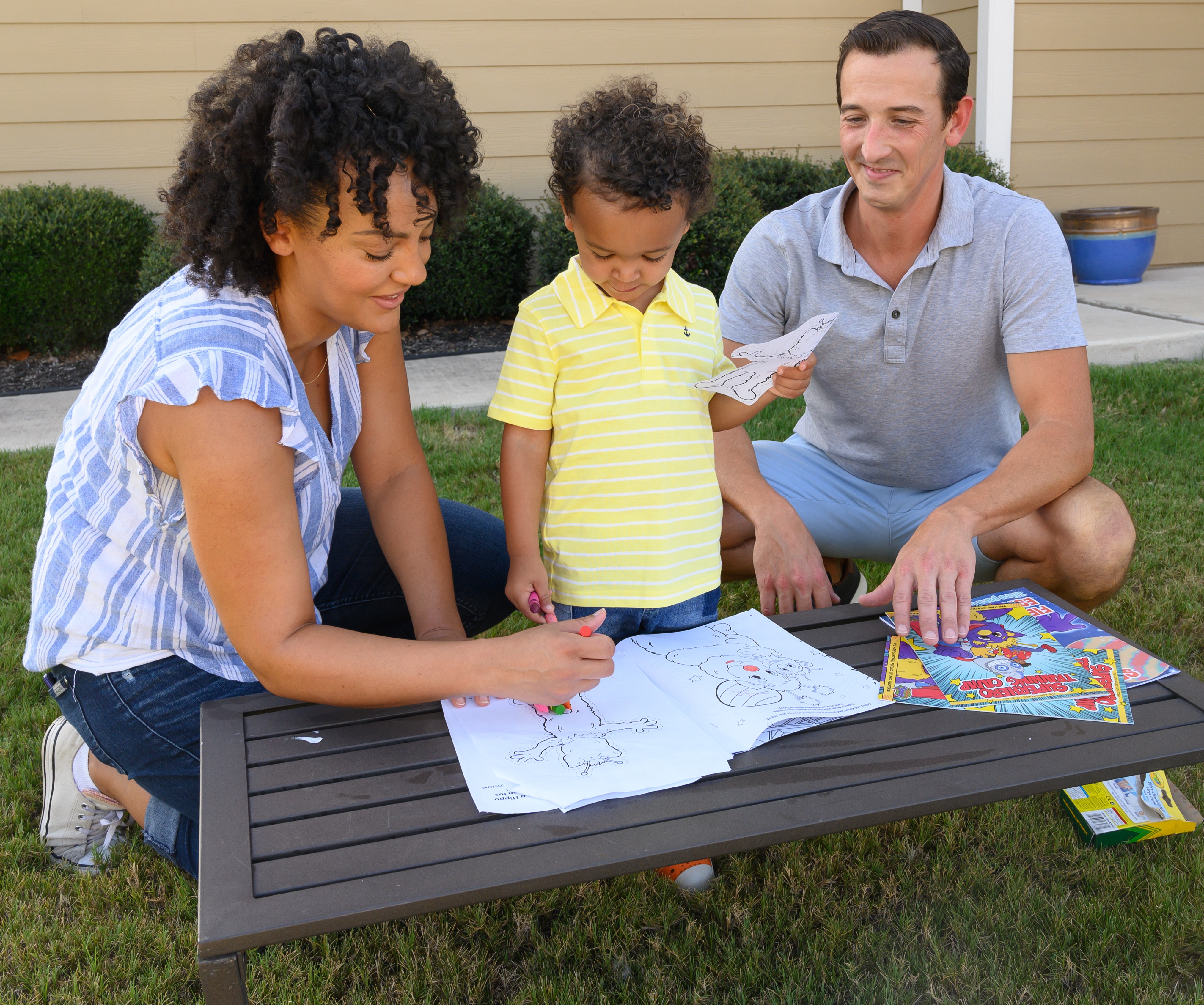A mom and dad coloring with their son outside. 